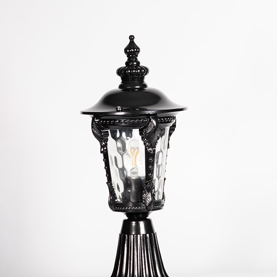 Closeup of black pillar light showing ornate frame design and patterned clear glass for stylish vintage outdoor lighting.