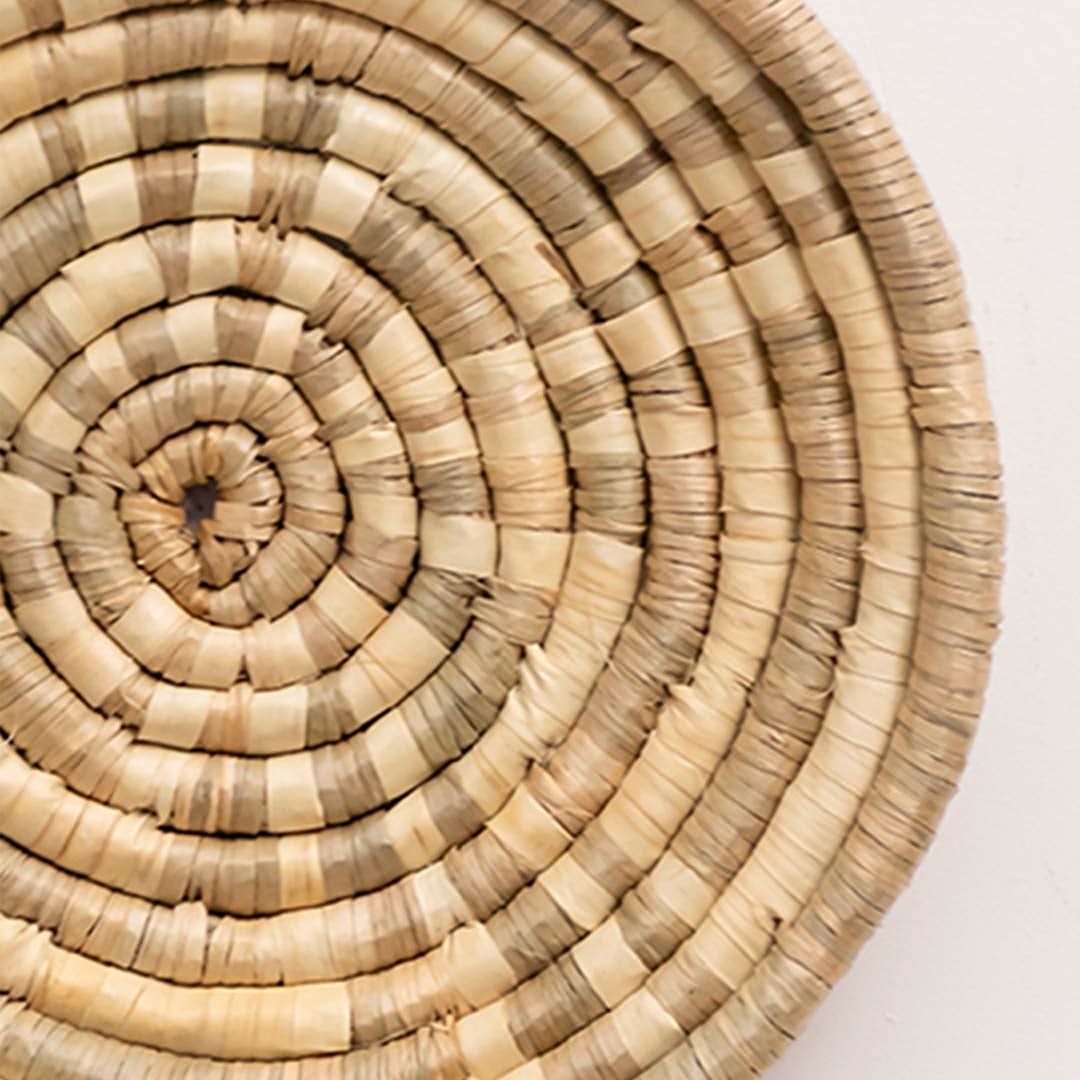 Closeup of handwoven wall basket showing tightly coiled natural fiber texture highlighting artisan craftsmanship and decor detailing.