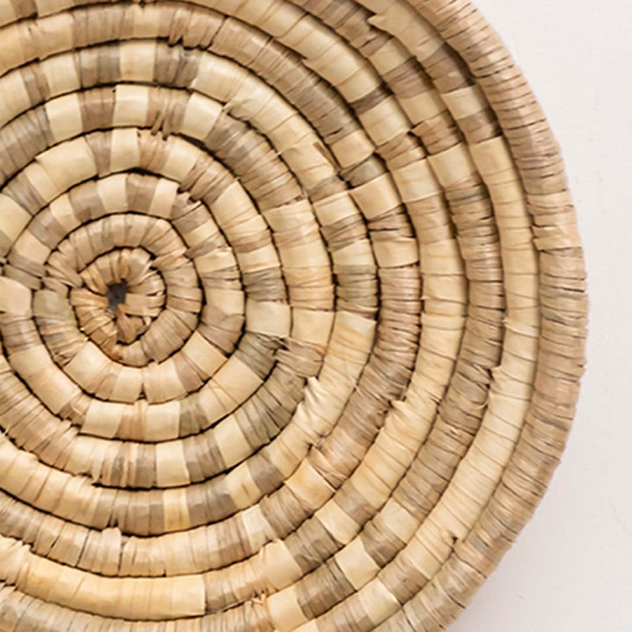 Closeup of handwoven wall basket showing tightly coiled natural fiber texture highlighting artisan craftsmanship and decor detailing.