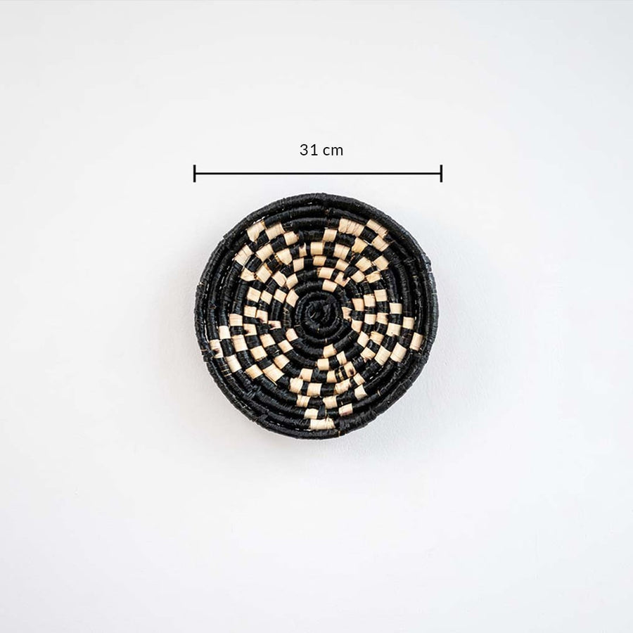 Handwoven round wall basket in black and natural fiber showing approx 25 cm diameter for accurate wall decor placement reference.