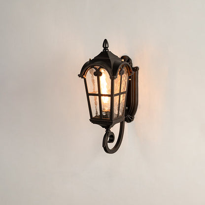 Black metal outdoor wall light on white background with a textured water glass shade and ornate bottom scroll design.