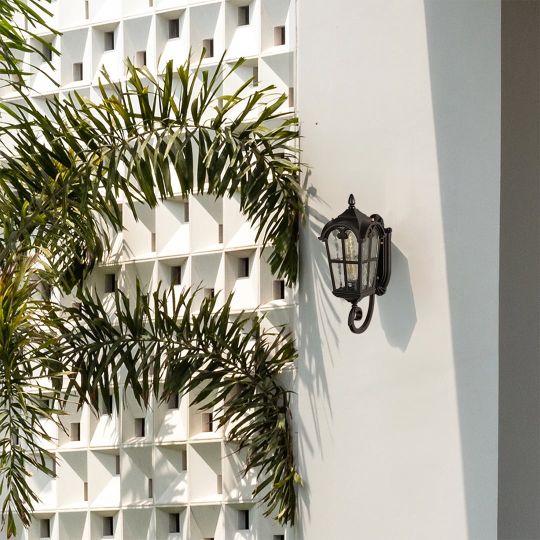 Black metal outdoor wall lantern lifestyle image with textured glass panels mounted on white modern villa wall near palms.