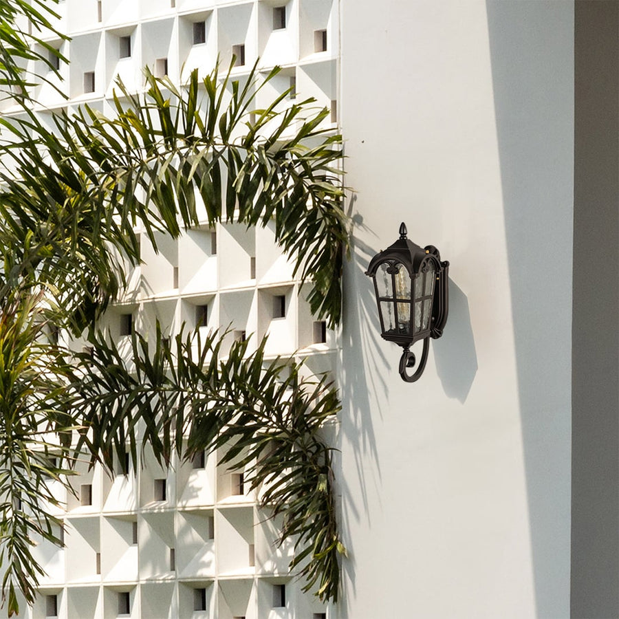 Black metal outdoor wall lantern lifestyle image with textured glass panels mounted on white modern villa wall near palms.