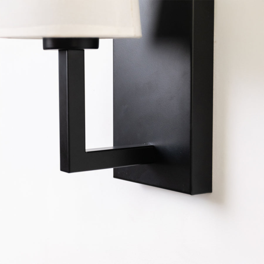 Closeup wall light in black metal finish with rectangular frame for bedroom or living decor lighting white background.