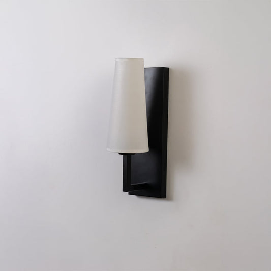 Black metal wall light with tall white fabric shade on a white background with light off highlighting its sleek modern vertical design.