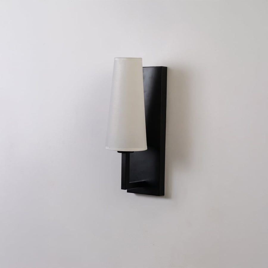 Black metal wall light with tall white fabric shade on a white background with light off highlighting its sleek modern vertical design.