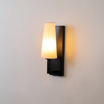 Black metal wall light with tall white fabric shade glowing softly on a clean white background ideal for modern bedroom or hallway lighting.
