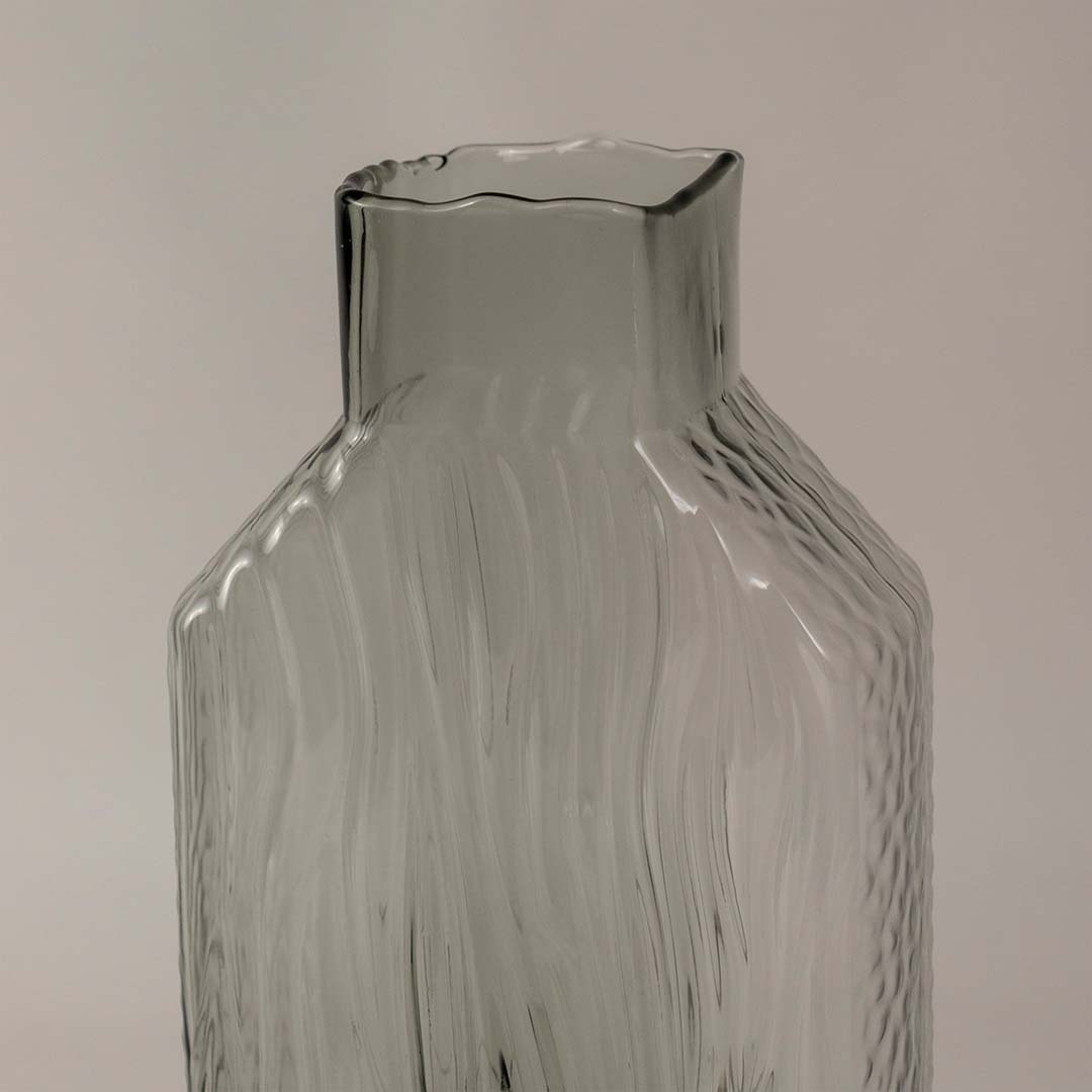 Closeup of tall smoky gray glass vase highlighting its wavy texture  glossy surface  and sleek geometric silhouette.