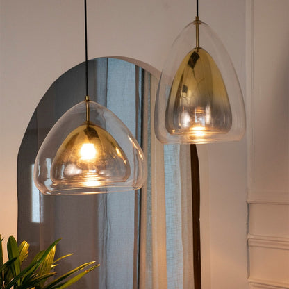 Warm pendant lights glowing in a cozy room setting with sheer curtains and indoor plants creating a soft inviting ambiance around the golden glass fixtures.