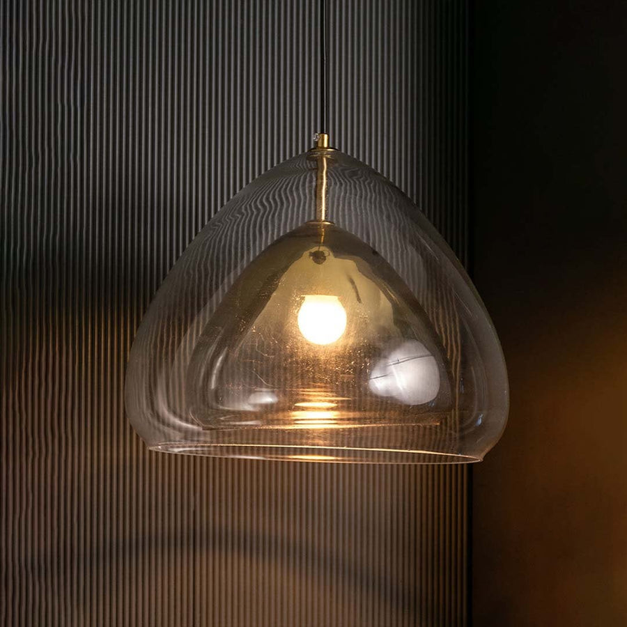 Golden glass pendant light turned on against a dark black background creating a striking warm illumination that highlights the curved glass design.
