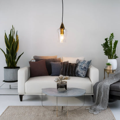A modern glass pendant light with a gold top illuminating a white sofa with mixed cushions and plants creating a soft stylish living room setting.