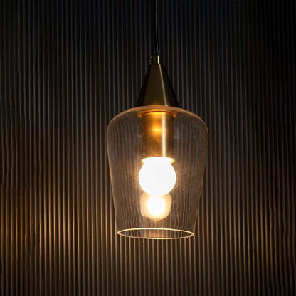 A clear glass pendant light with a gold top glowing warmly against a black textured backdrop.