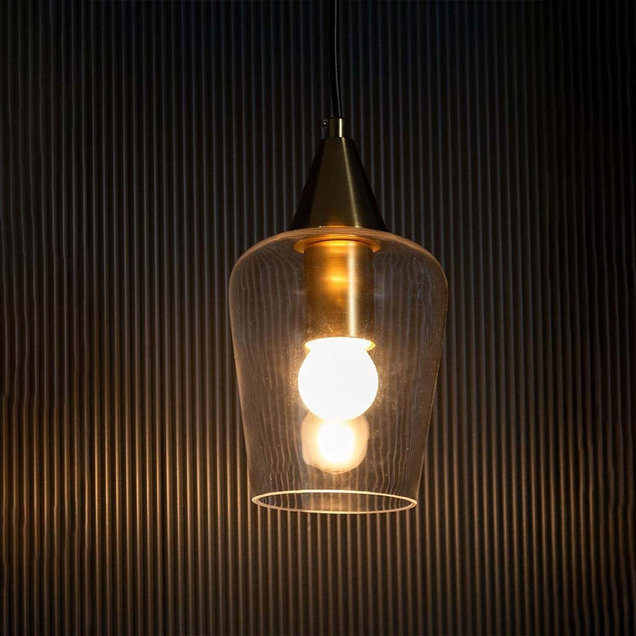 A clear glass pendant light with a gold top glowing warmly against a black textured backdrop.