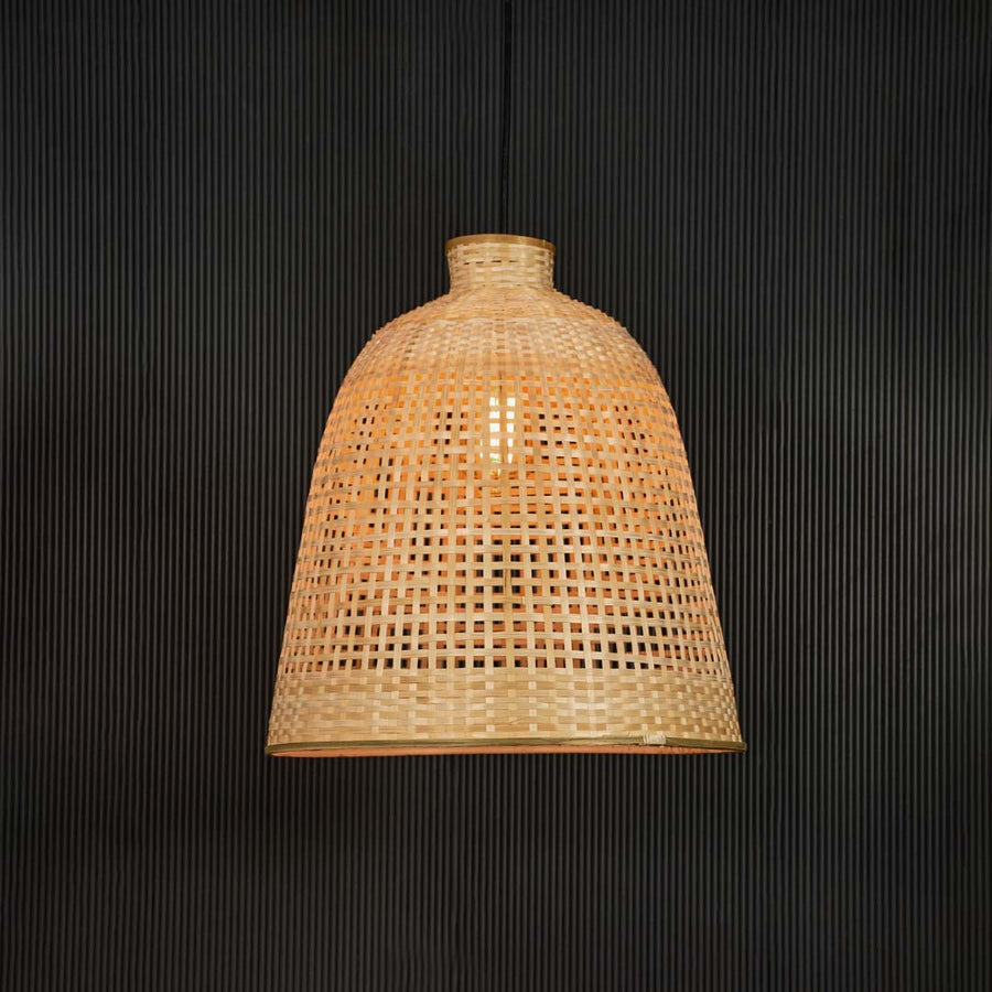 Handwoven rattan pendant light with tall bamboo shade turned on glowing softly against black background.