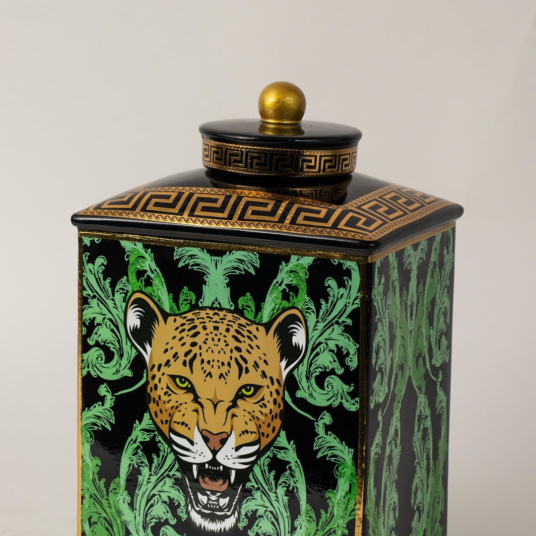 Closeup of black ceramic jar showing gold lid and detailed hand-painted leopard with leaf accents.