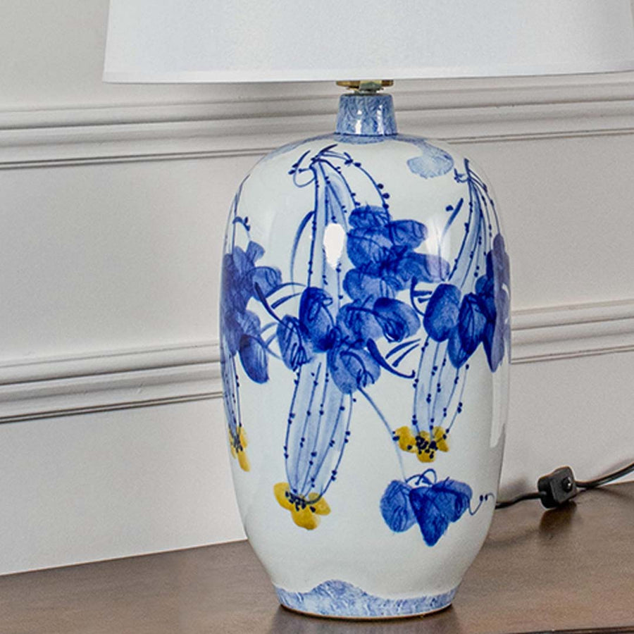 Closeup of white ceramic lamp with detailed blue floral artwork and white shade showcasing refined craftsmanship and classic artistic beauty.