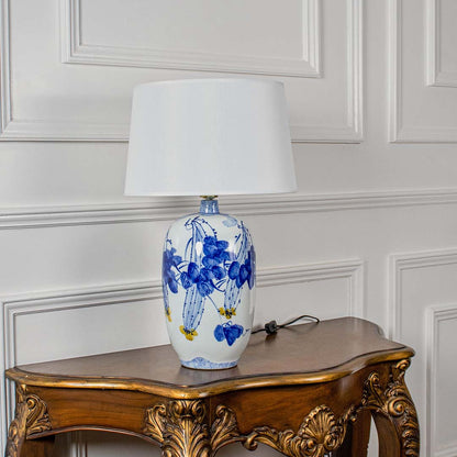 White ceramic lamp with blue floral artwork and white shade shown unlit on a clean white background highlighting its elegant artistic design.