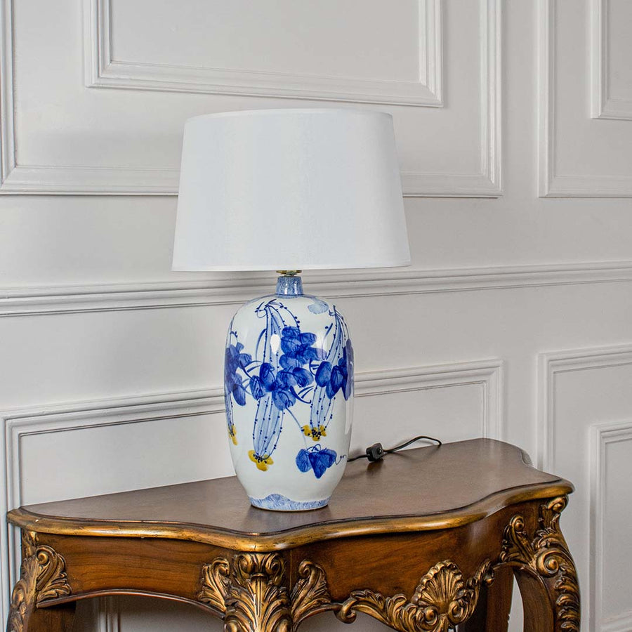 White ceramic lamp with blue floral artwork and white shade shown unlit on a clean white background highlighting its elegant artistic design.