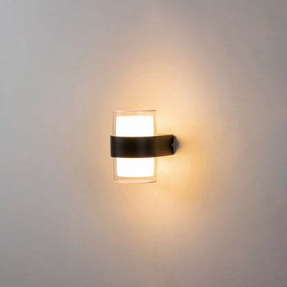 Modern black wall light glowing on white wall with frosted glass shade for elegant ambient interior decor.