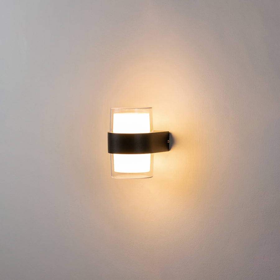 Modern black wall light glowing on white wall with frosted glass shade for elegant ambient interior decor.