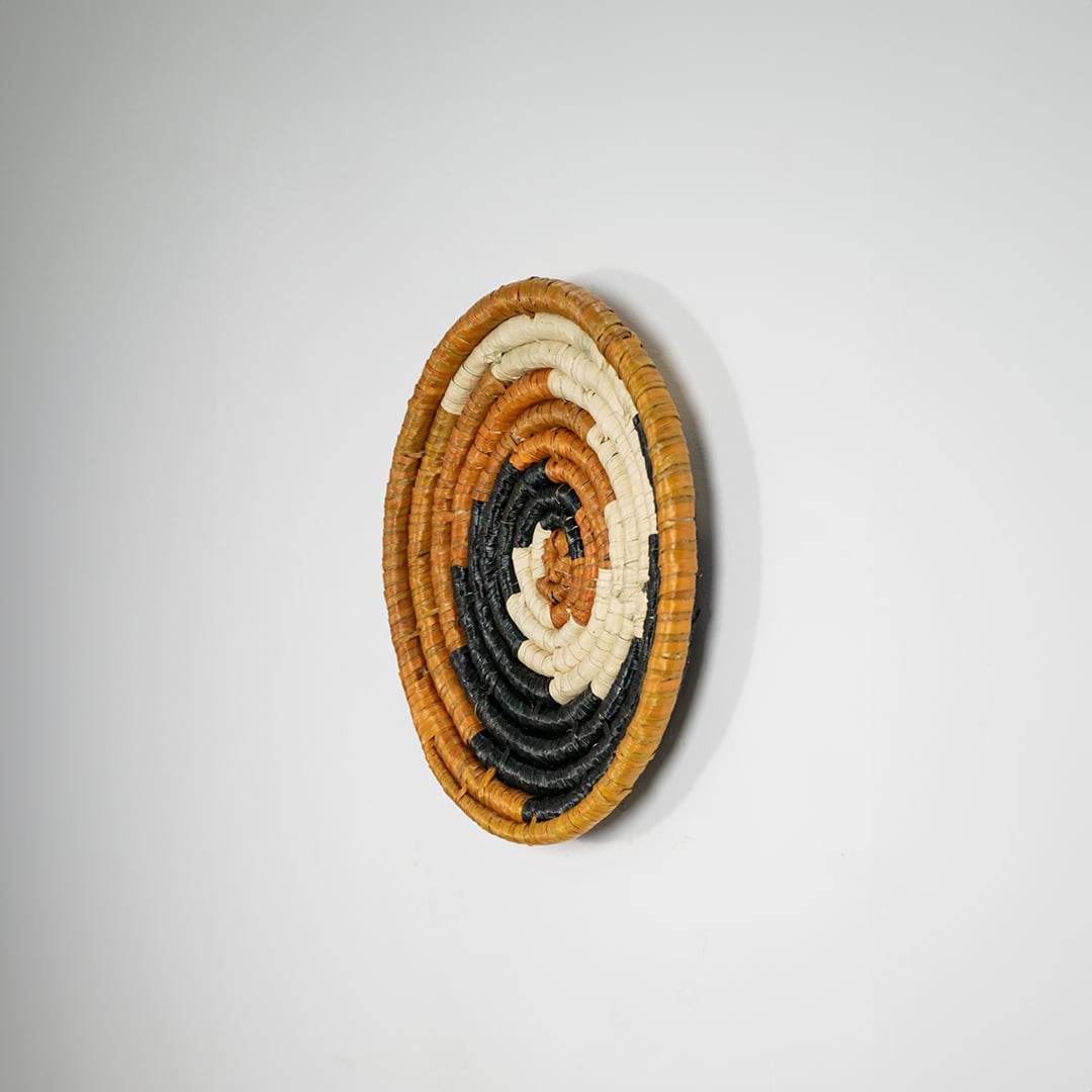 Round jute and black woven wall basket decor handmade rustic boho spiral design wall art accent piece shown from side view.