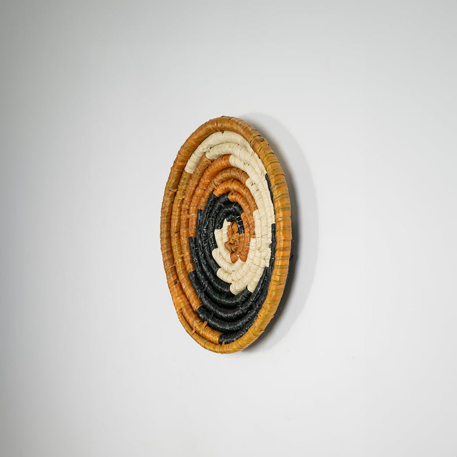 Round jute and black woven wall basket decor handmade rustic boho spiral design wall art accent piece shown from side view.