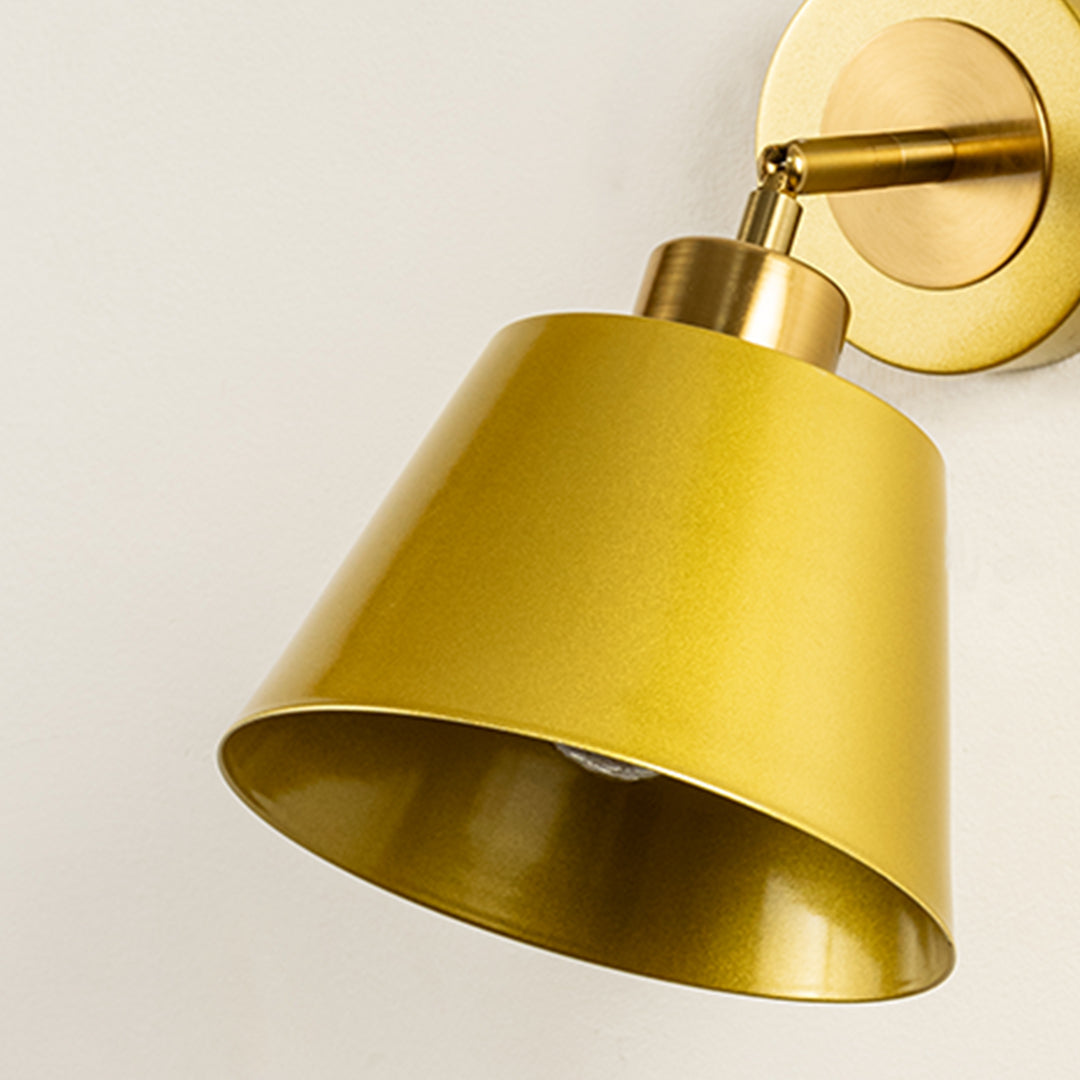 Closeup of gold metal wall light with cone shade showcasing smooth finish and premium detailing for modern interior decor styling.