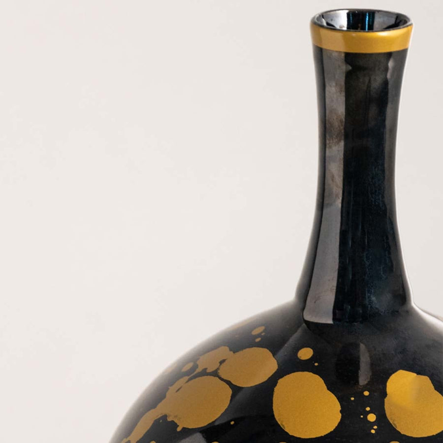 Detailed closeup of ceramic vase showing glossy black glaze with rich golden splatter patterns.