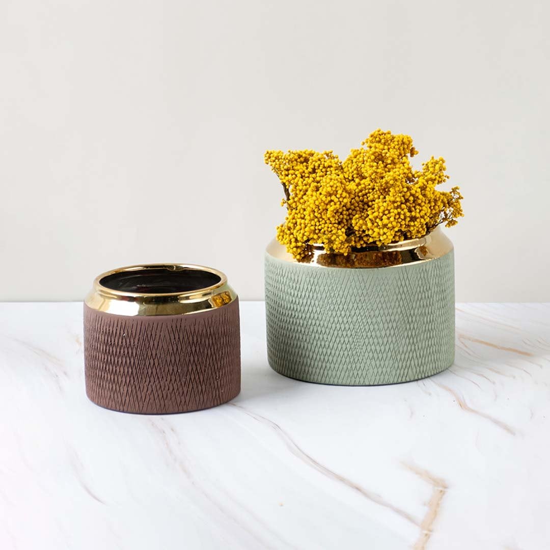 A brown vase with a gold rim displayed as part of a grouped decor setup highlighting its modern textured design and compact rounded form.