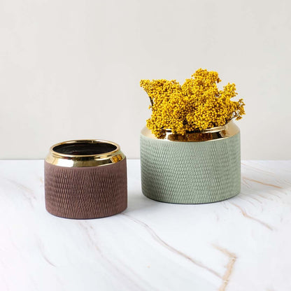 A brown vase with a gold rim displayed as part of a grouped decor setup highlighting its modern textured design and compact rounded form.