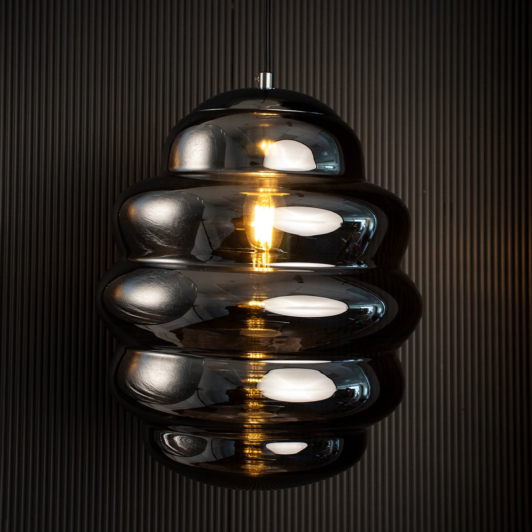 Ripple chrome pendant light glowing against dark background emphasizing reflective metallic layers and sculptural form.