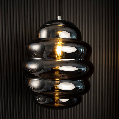 Ripple chrome pendant light glowing against dark background emphasizing reflective metallic layers and sculptural form.