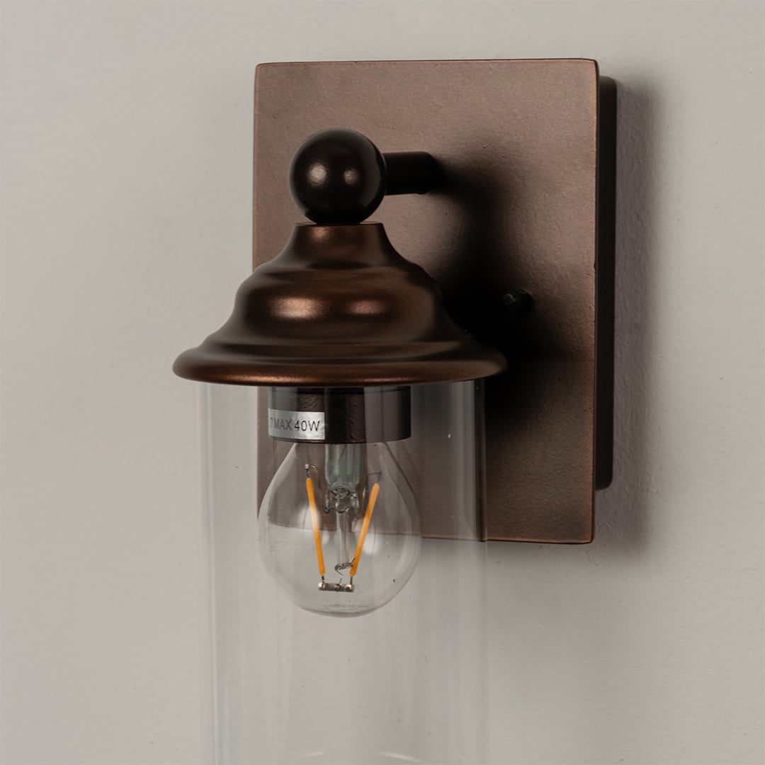 Closeup of bronze wall sconce showcasing the clear glass shade and warm filament bulb for ambient lighting.