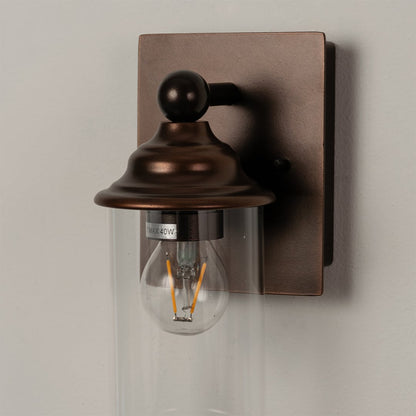 Closeup of bronze wall sconce showcasing the clear glass shade and warm filament bulb for ambient lighting.