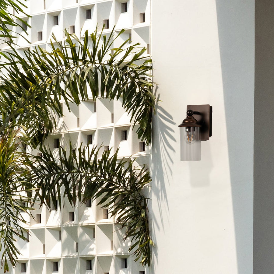 Bronze wall mounted light with clear cylindrical glass shade displayed on white background for decor detailing.