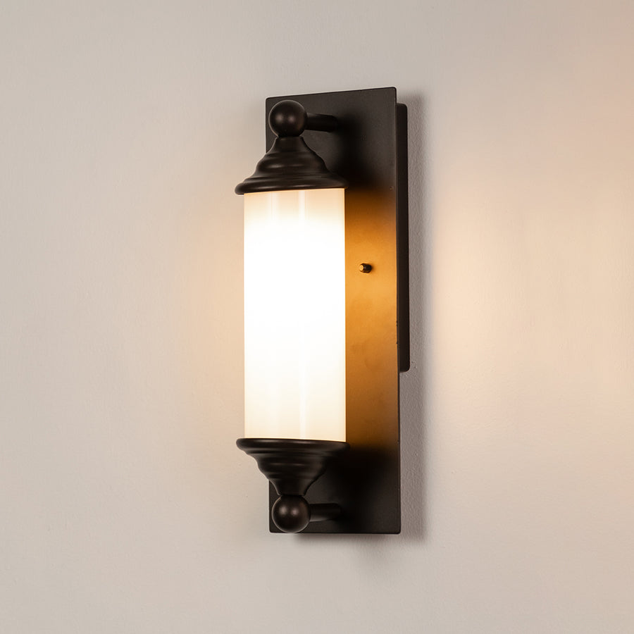 Black metal wall light on white background with frosted glass shade for elegant modern exterior decor.