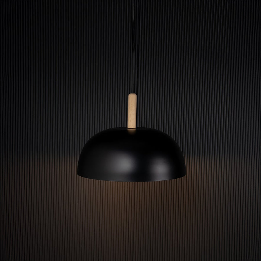 Black dome pendant ceiling light with wooden top illuminated on back background for dining room cafe and modern home interior lighting.