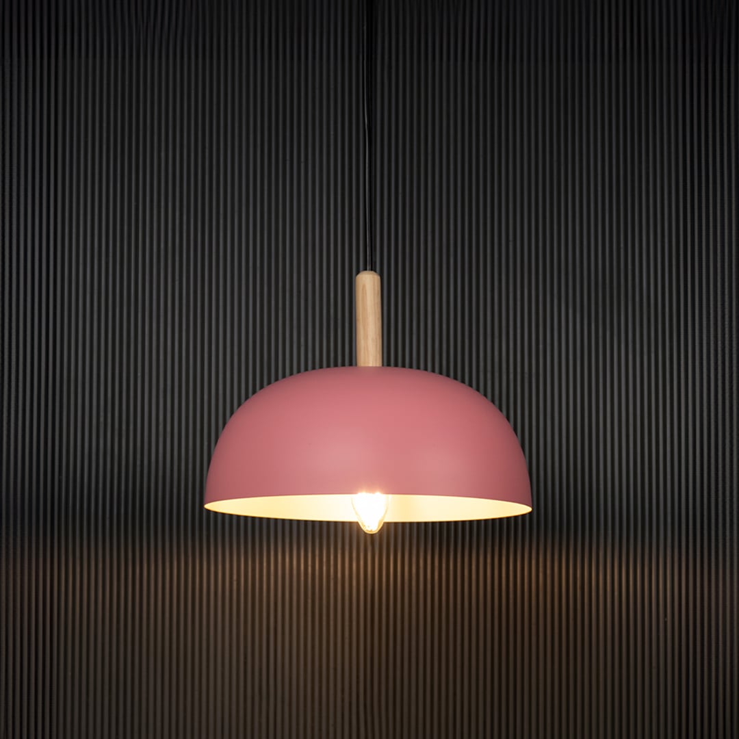 Pink dome pendant ceiling light with wooden detail illuminated on back background for modern home dining and cafe interior lighting.