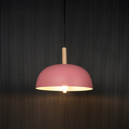 Pink dome pendant ceiling light with wooden detail illuminated on back background for modern home dining and cafe interior lighting.