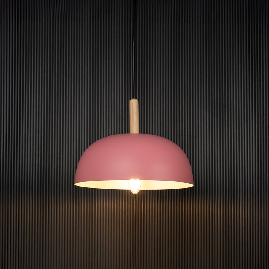 Pink dome pendant ceiling light with wooden detail illuminated on back background for modern home dining and cafe interior lighting.