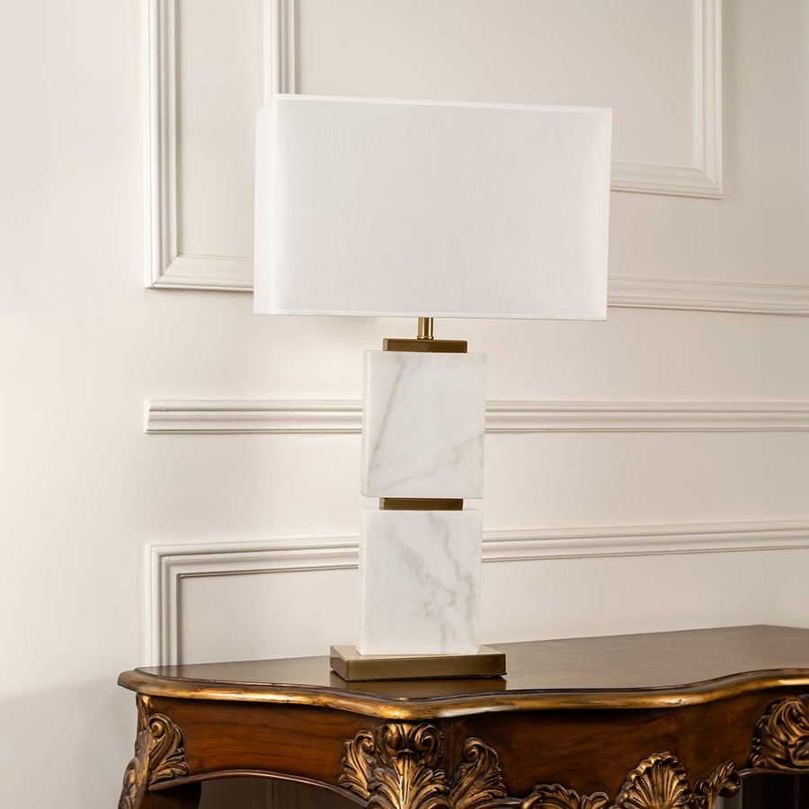 White shade marble block table lamp on carved console table with light off and white panel wall background for modern luxury décor.