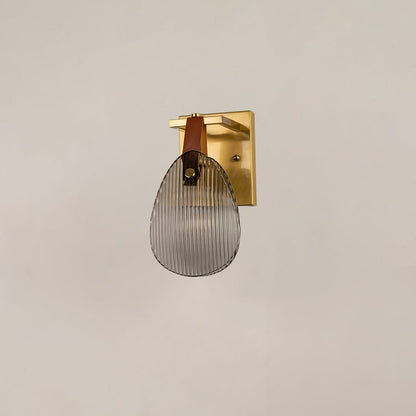 Gold metal wall sconce with ribbed glass and leather strap illuminated on white background for elegant lighting.