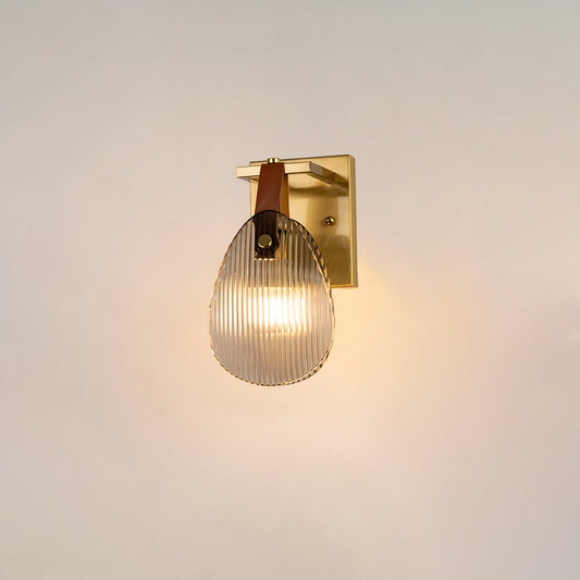 Gold wall light with ribbed glass shade and leather strap glowing on a white background for modern home lighting.