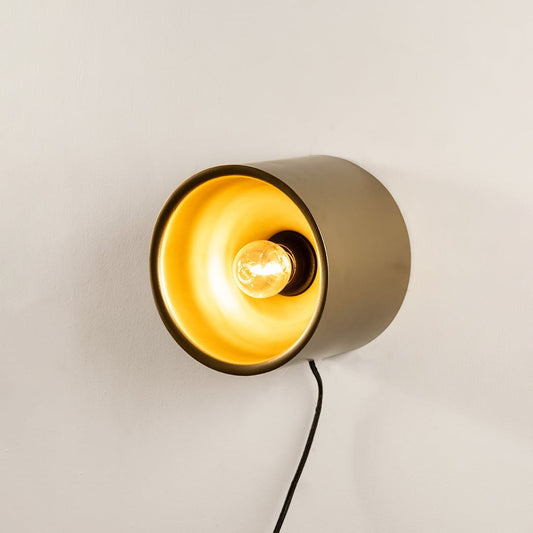 Contemporary matte gold metal cylinder wall light fixture turned on showing a bright golden interior illumination.