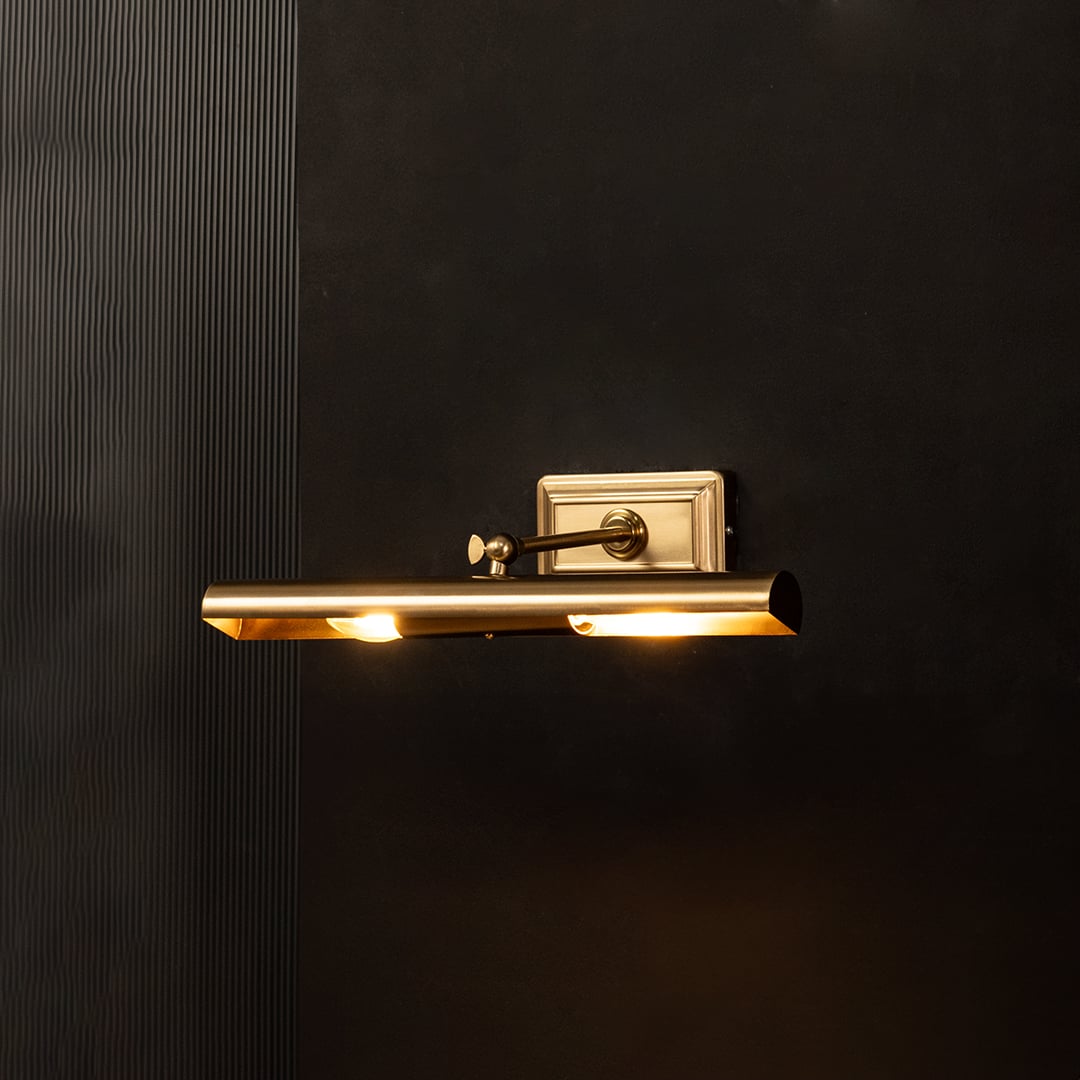 Gold metal picture light glowing warmly on a black background creating a dramatic accent lighting effect.