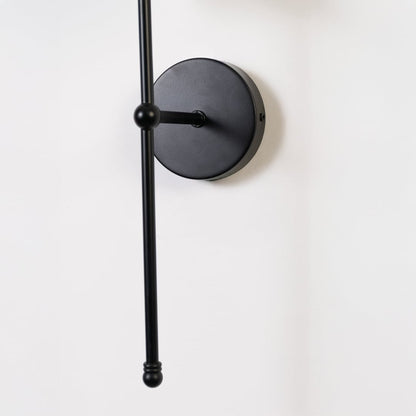 Closeup of black wall light showing the slim metal rod and white shade with a modern minimal finish.