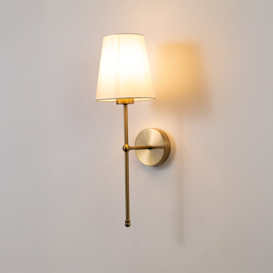 Wall light with a gold metal frame and white fabric shade glowing softly on a clean white background.