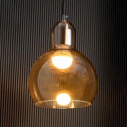 Amber glass pendant light glowing warmly with visible bulb gold metal holder creating ambient lighting on dark wall.