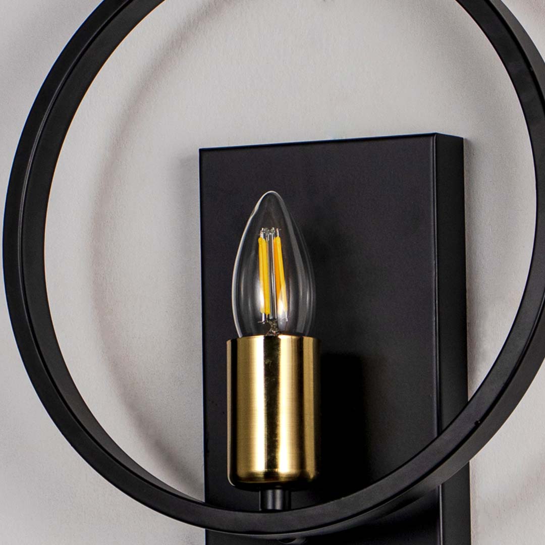 Modern wall light with circular black frame and gold holder with filament bulb on neutral background decorative lighting for interiors.