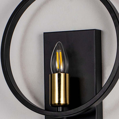 Modern wall light with circular black frame and gold holder with filament bulb on neutral background decorative lighting for interiors.